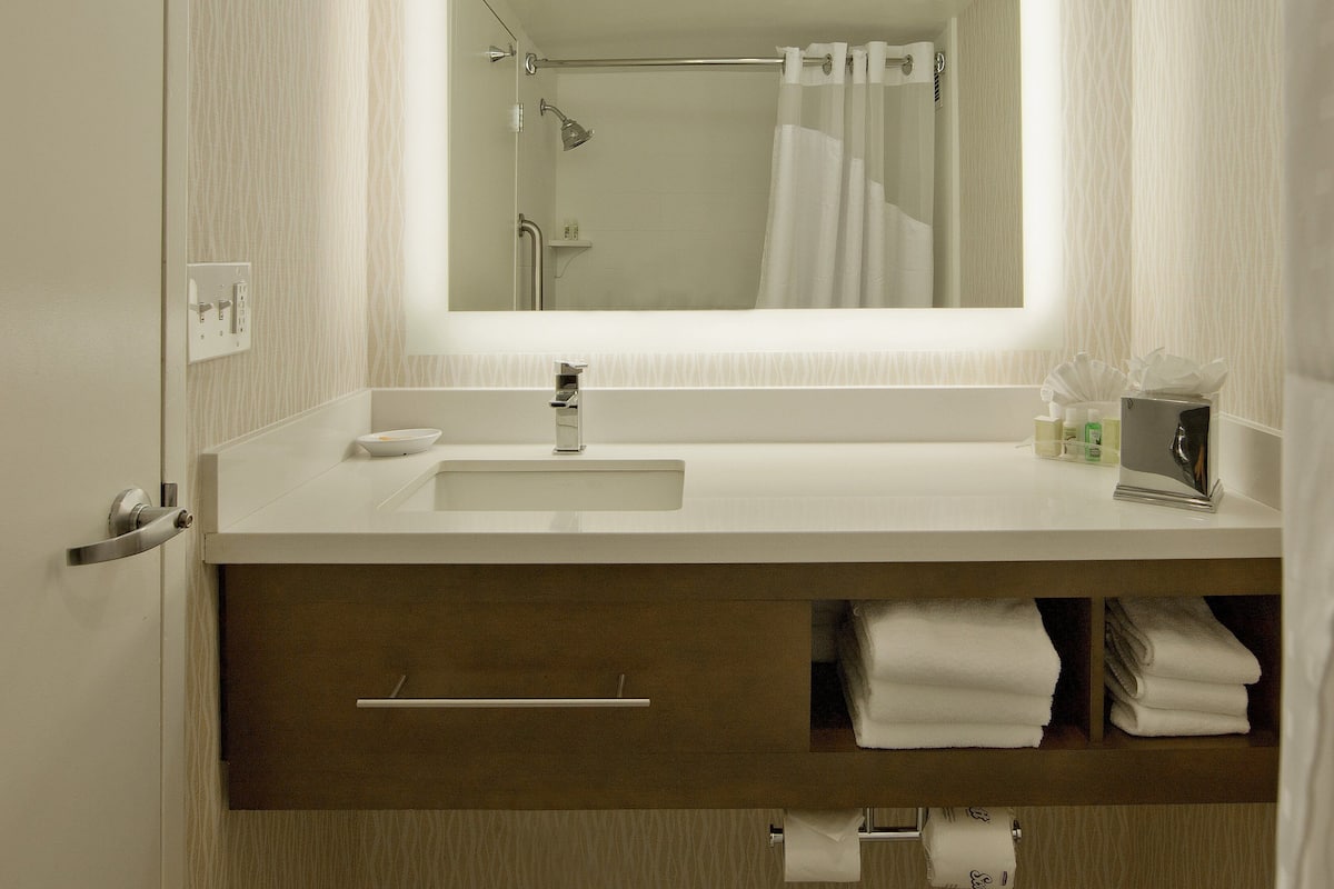 Un baño con un lavabo blanco, un espejo, ducha y toallero.