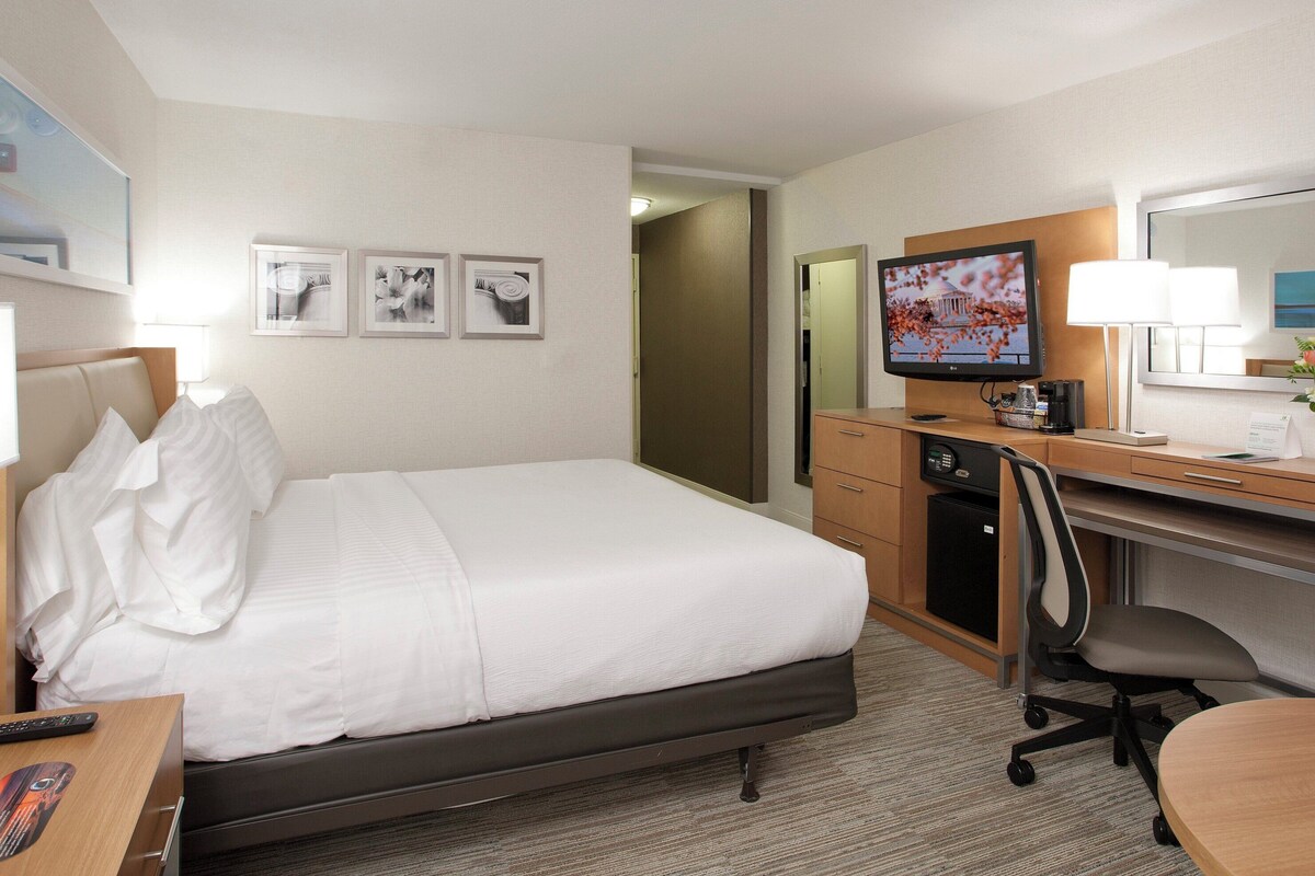 Une chambre d’hôtel équipée d’un lit, d’un bureau, d’une chaise, d’une télévision et d’une petite kitchenette.