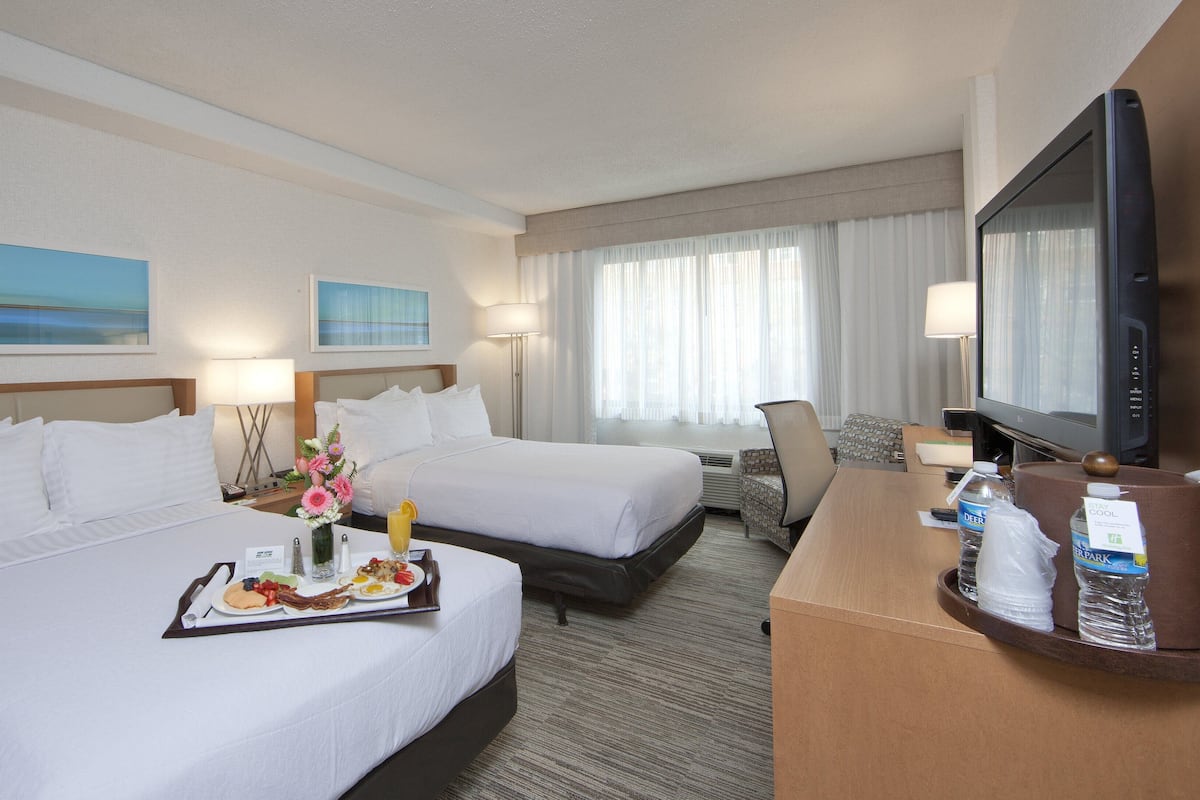 Habitación de hotel con dos camas, un escritorio, un televisor y una mesa de comedor con desayuno.