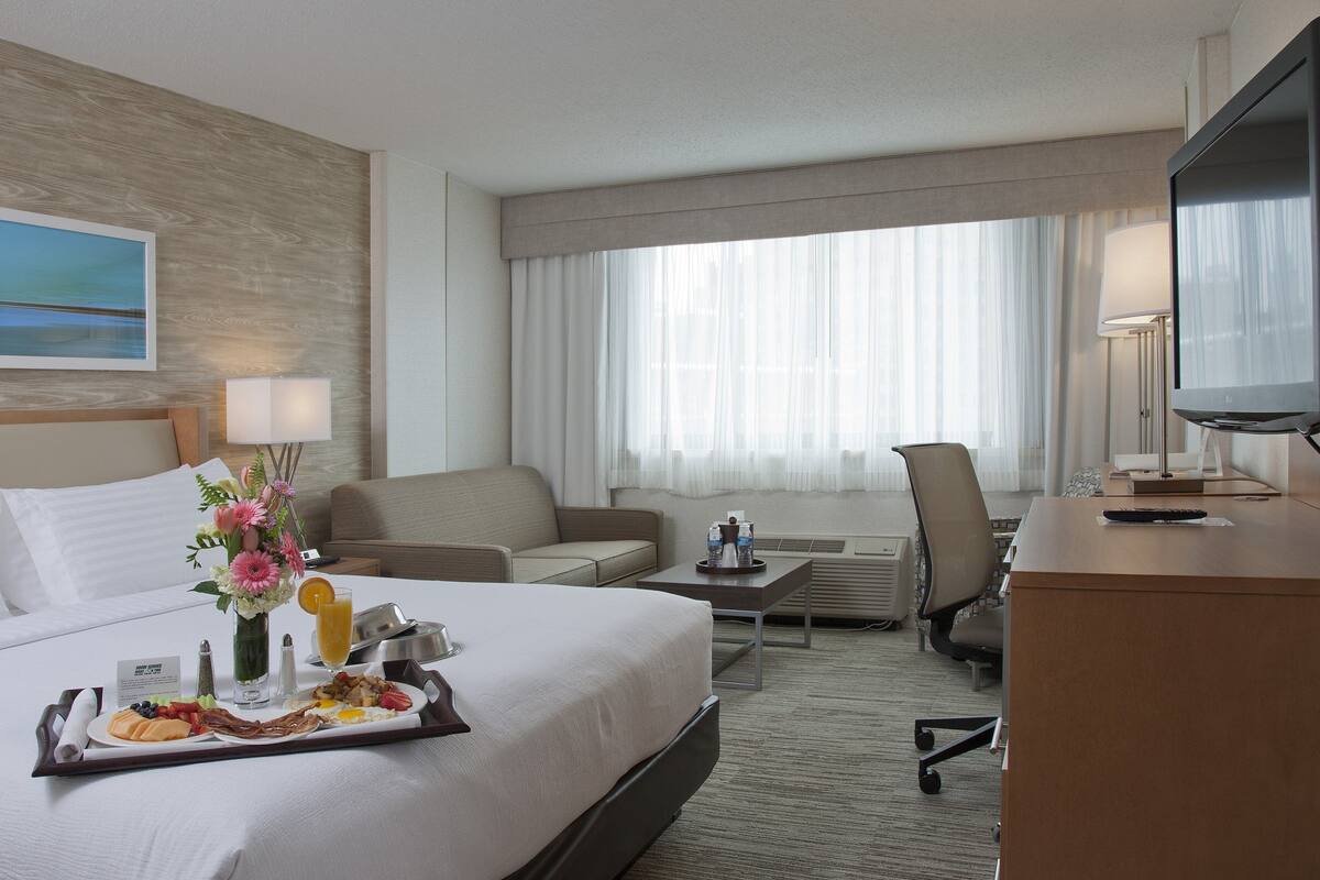 Habitación de hotel con cama, escritorio, silla, televisor y ventana con cortinas.
