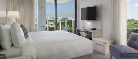A modern hotel room with a large bed, a desk with a chair, a flat-screen TV, and a city view.
