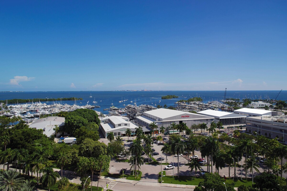 A marina with boats, a large building with a flat roof, and palm trees.