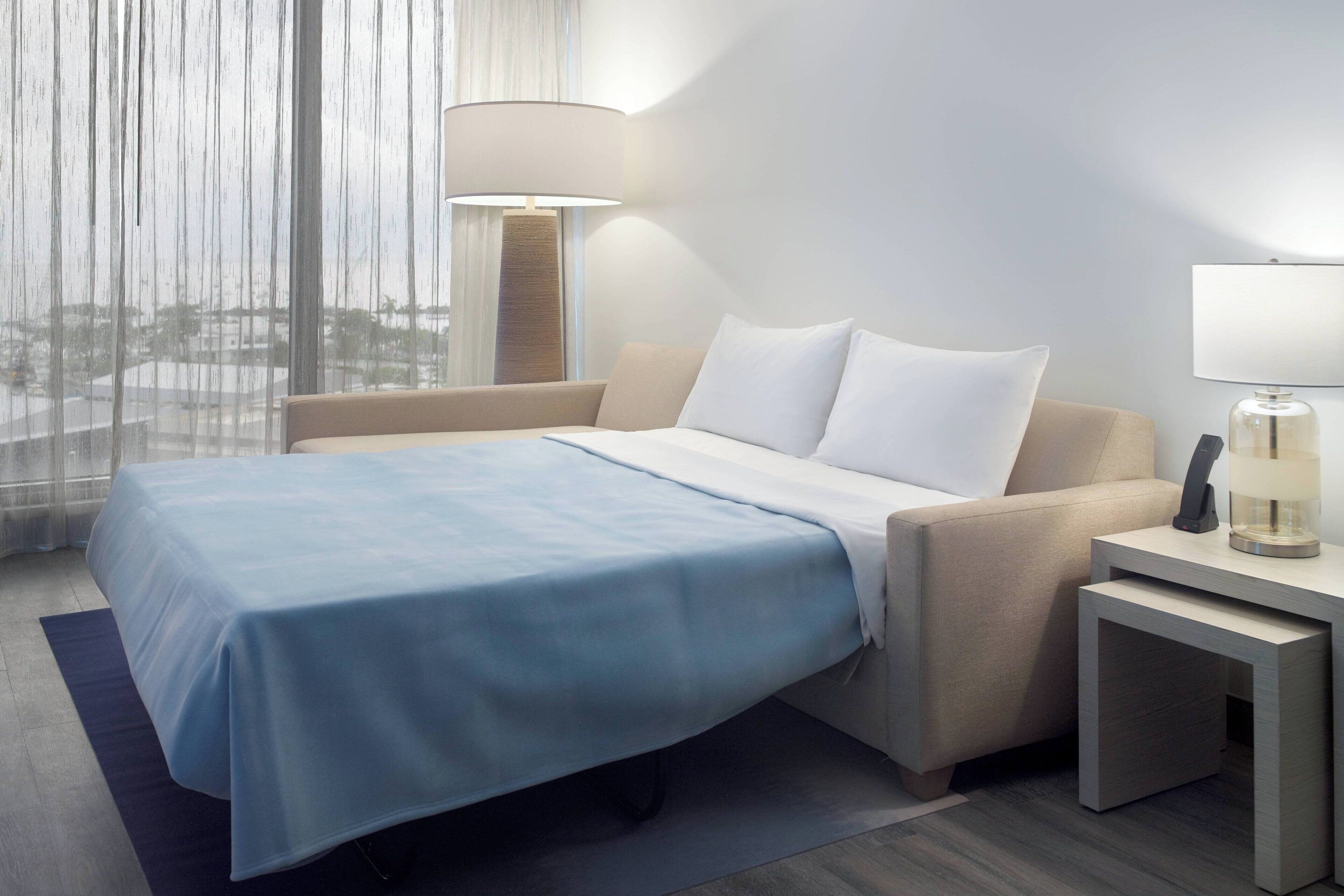 A hotel room with a bed, a nightstand, a lamp, and a view through the window.