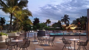 A rooftop bar with outdoor seating, a pool, and palm trees.