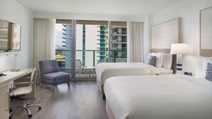 A hotel room with two beds, a desk, a chair, and a TV.