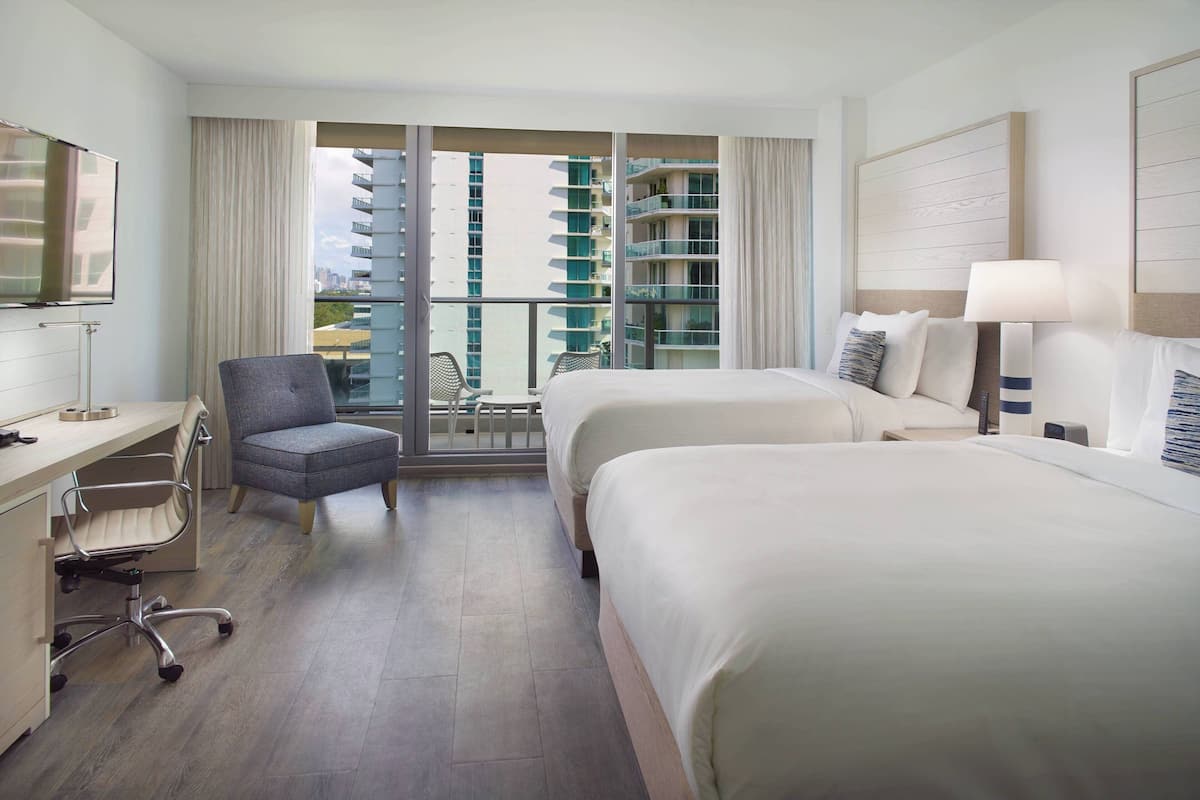 A hotel room with two beds, a desk, a chair, and a TV.