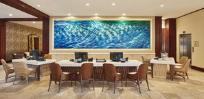 A conference room with a large painting of a blue ocean, two Laptops, and wicker chairs.