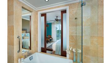 A bathroom with a bathtub, a shower, and a glass door leading to a balcony with a bed and a table.