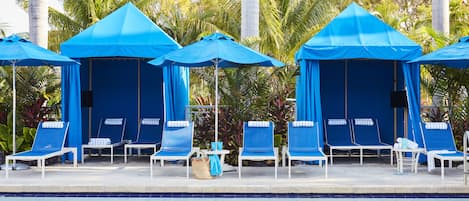 A poolside area with blue canopies, lounge chairs, and a tiled pool.