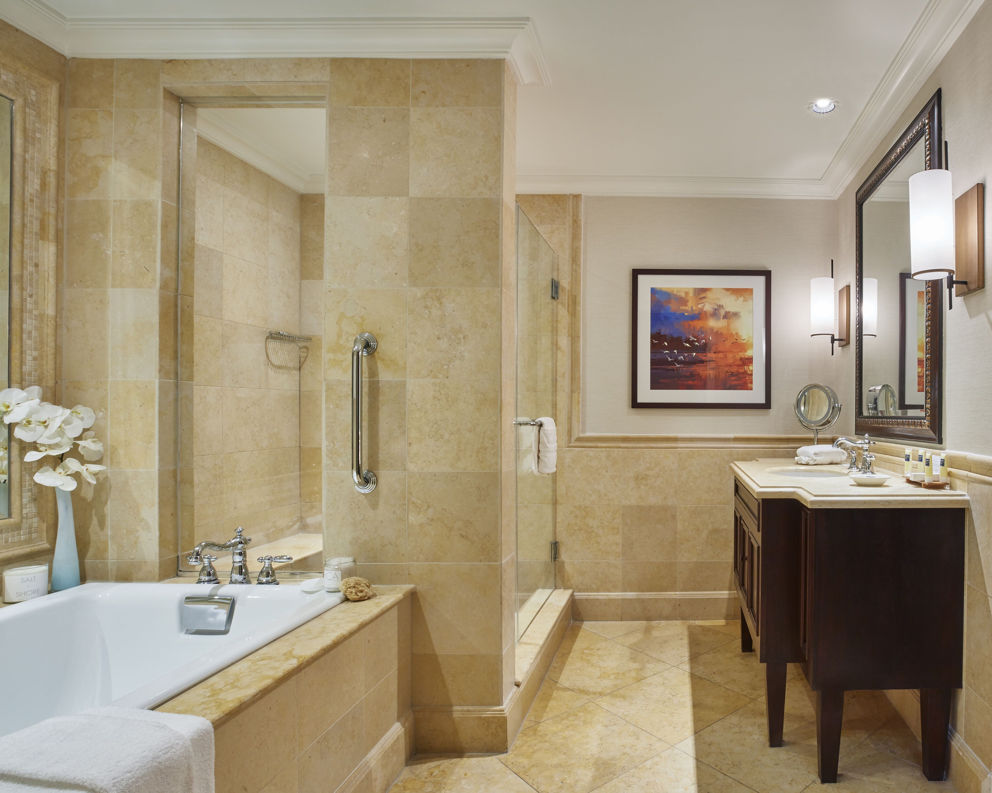 A modern bathroom with a bathtub, a shower with a glass door, a vanity with a mirror, and a framed painting on the wall.