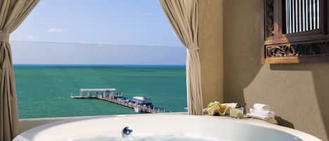 A bathroom with a large bathtub, a view of the sea, and a pier with boats.
