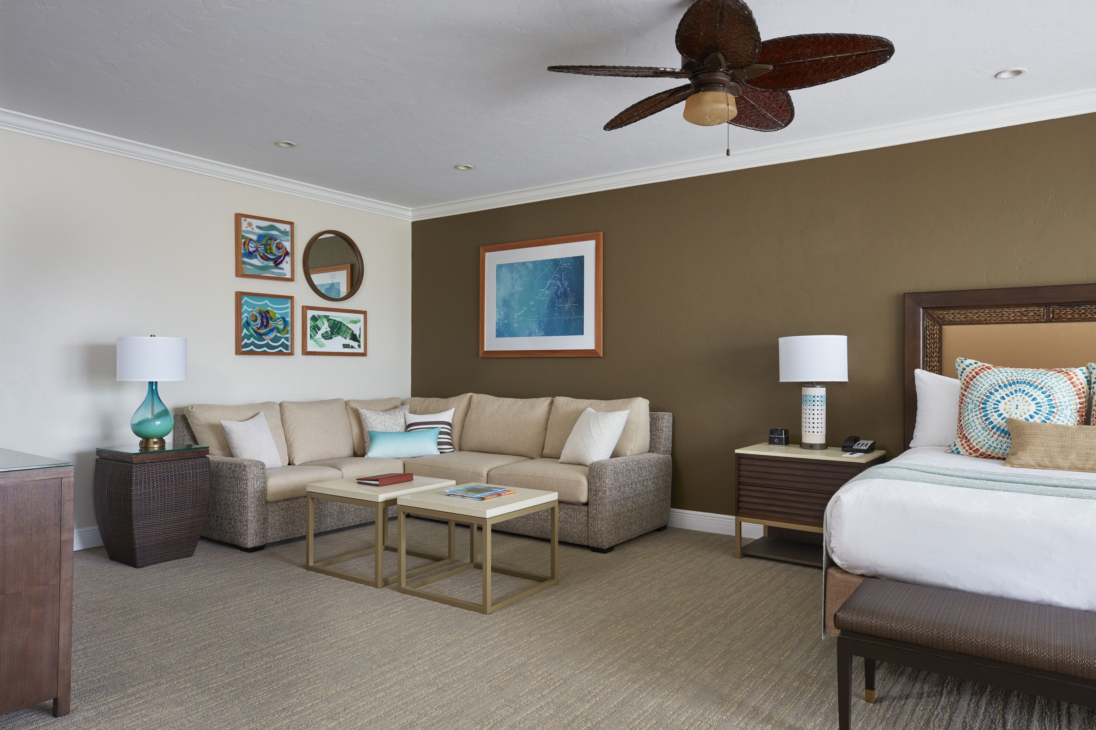 A hotel room with a bed, a sofa, a coffee table, a nightstand, and a ceiling fan.