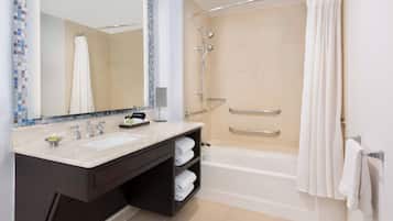 Un baño moderno con bañera, ducha, un espejo grande y tocador con lavamanos y toallero.