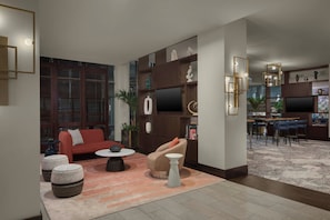 Un salon moderne avec un canapé rouge, un fauteuil beige et une table basse. On aperçoit à l’arrière-plan un coin cuisine avec une table à manger et des chaises.