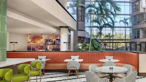 A modern hotel lobby with a high ceiling, a central seating area with a red bench, and a bar counter.