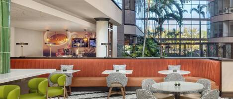 A modern hotel lobby with a high ceiling, a central seating area with a red bench, and a bar counter.