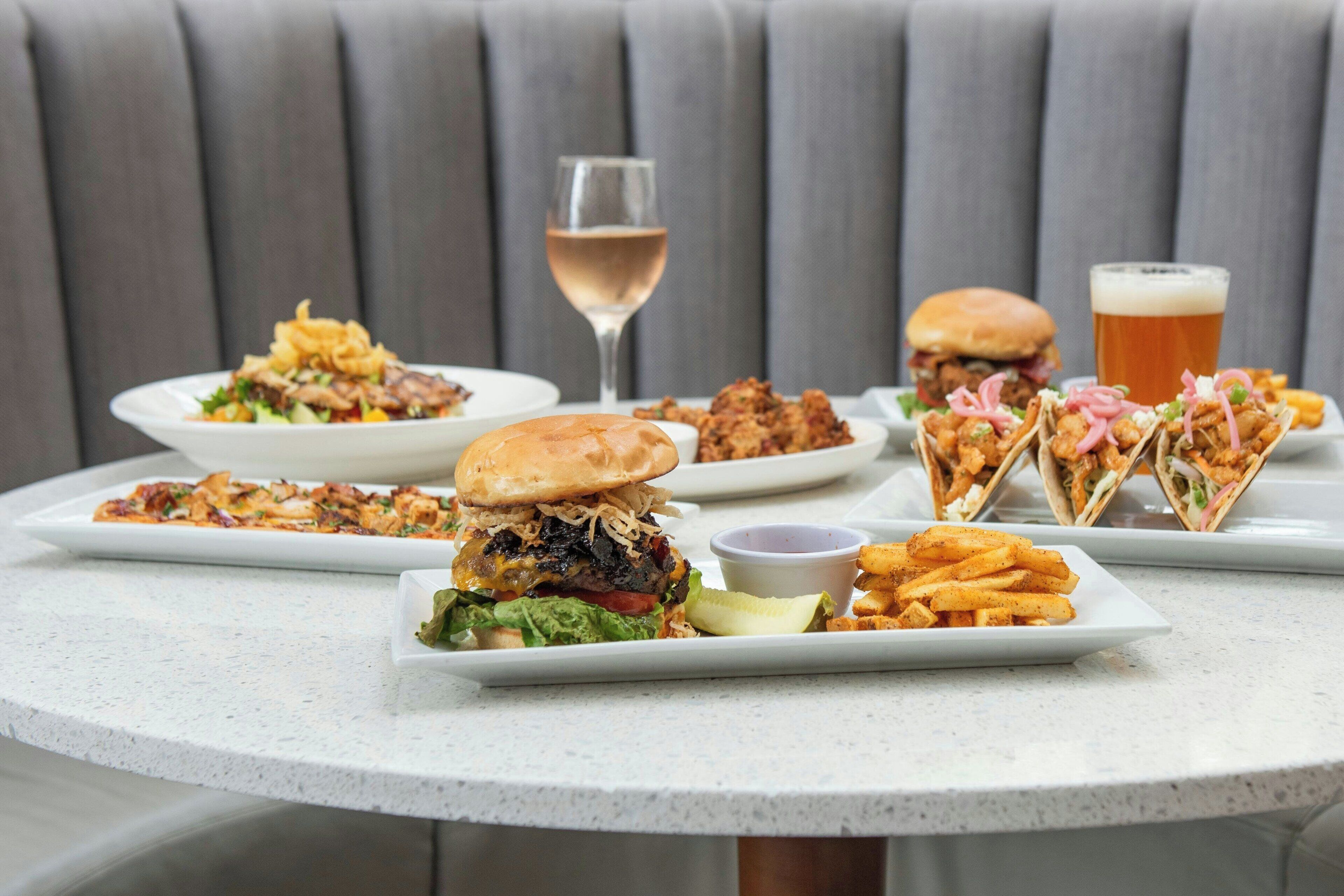 A table with various dishes including burgers, tacos, and fries, accompanied by drinks.
