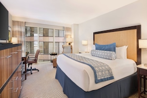 Ein Hotelzimmer mit einem großen Bett, einem Schreibtisch, einem Stuhl und einem Fernseher.