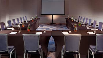 A conference room with a large screen, long tables, and chairs arranged for meetings.