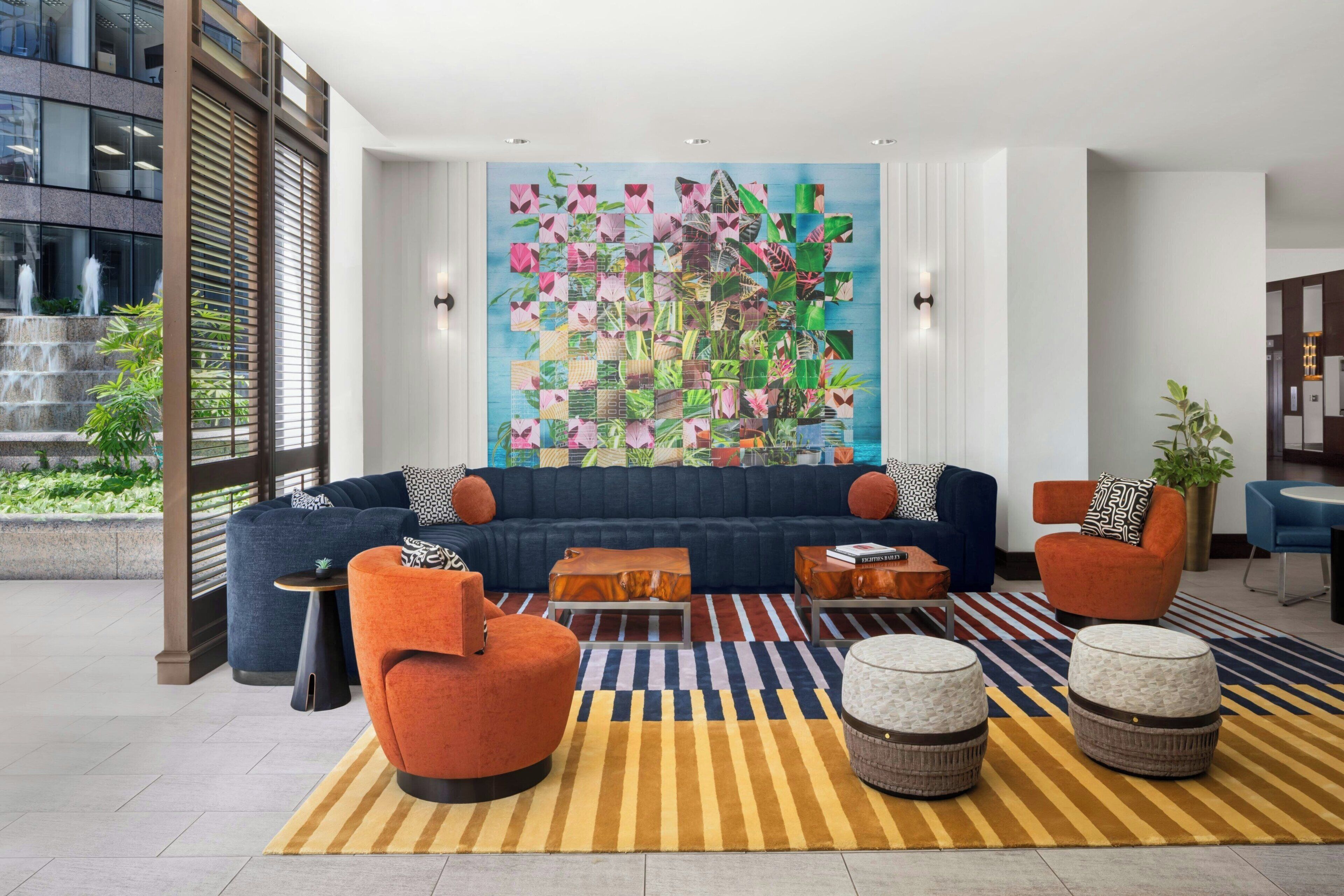 Un área de estar moderna con un sofá azul, sillones naranja y un cuadro abstracto de colores.