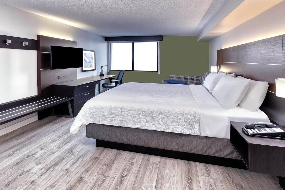 Ein modernes Hotelzimmer mit einem großen Bett, einem Schreibtisch mit Flachbildfernseher, einer Sitzecke mit Sofa und einem Fenster mit Blick.