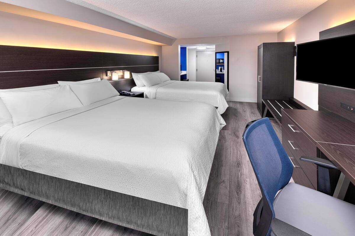 Ein Hotelzimmer mit zwei Betten, einem Schreibtisch, einem Stuhl, einem Fernseher und einem durch eine offene Tür einsehbaren Badezimmer.
