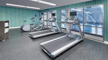 Un gimnasio con cintas de correr, bicicletas estáticas y un estante de mimbre con toallas.