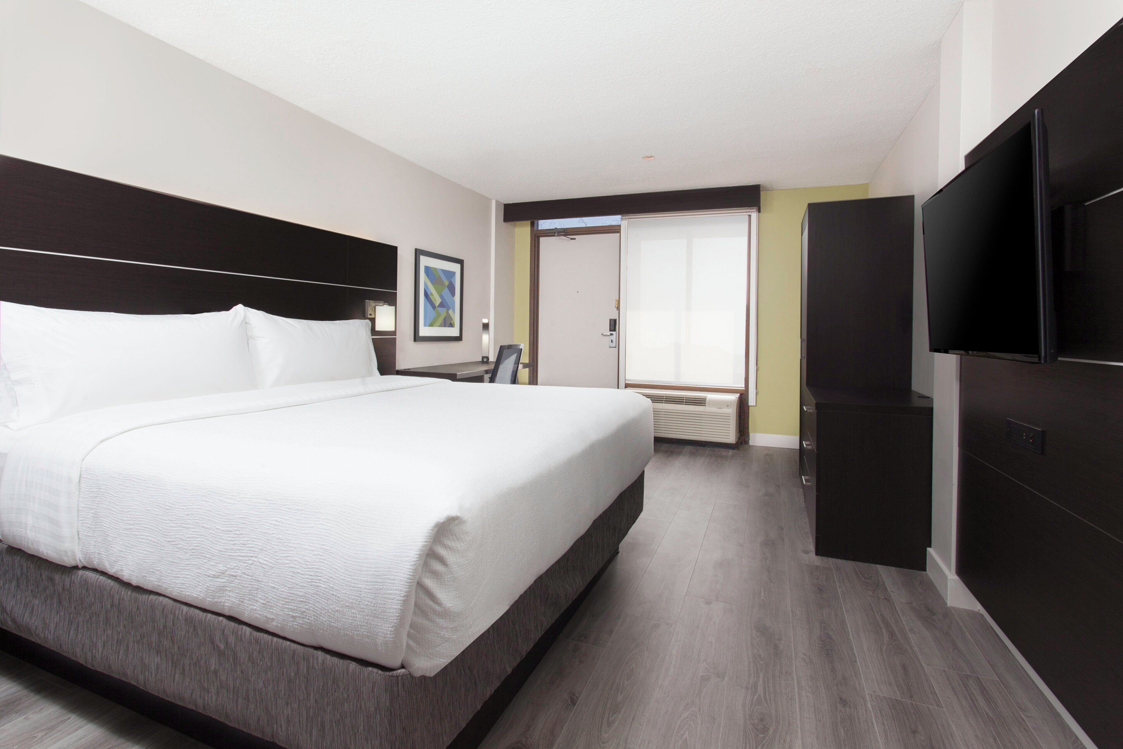 Une chambre d’hôtel avec un grand lit, un téléviseur à écran plat, une armoire et une porte donnant sur un balcon.