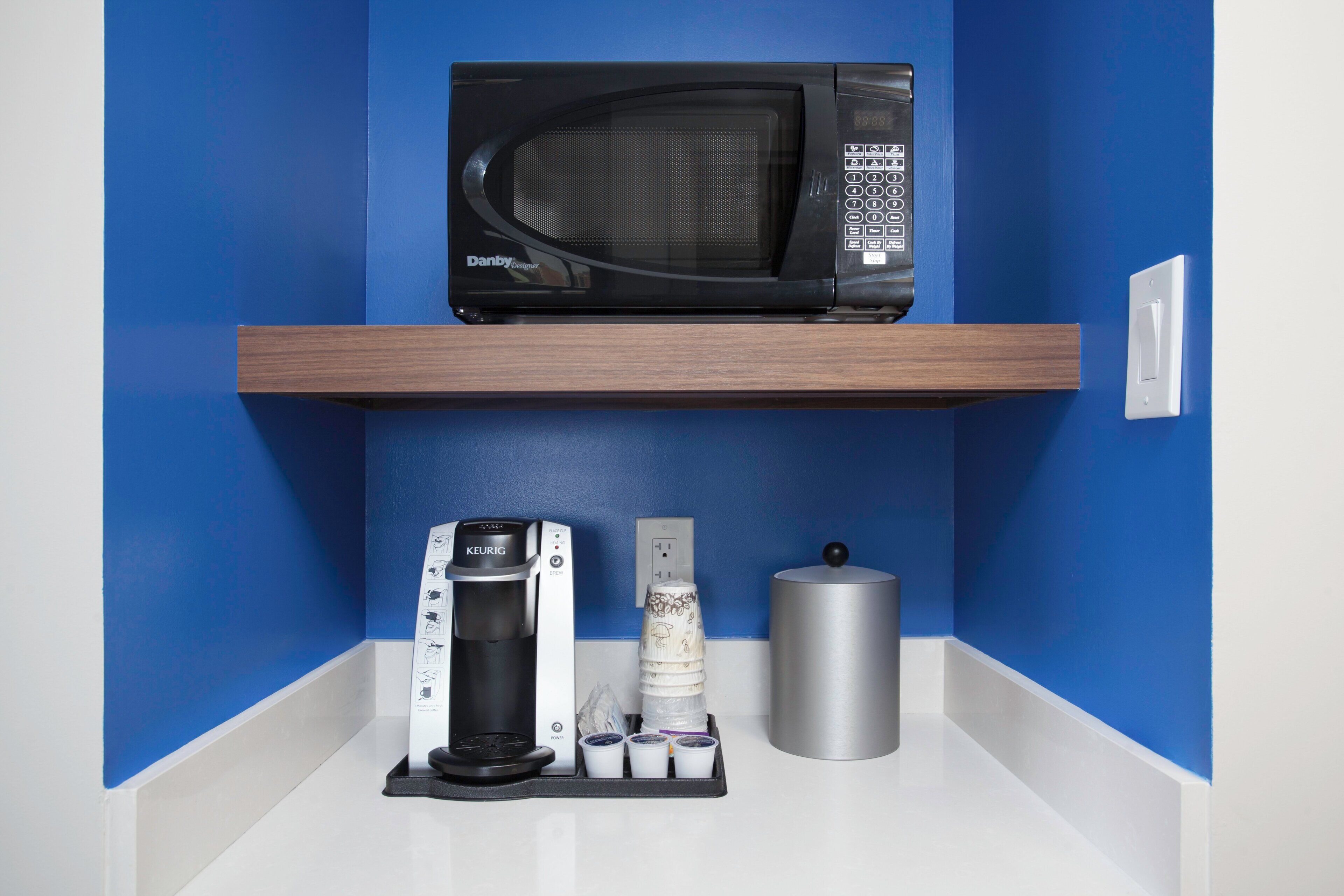 A kitchen area with a microwave on a shelf, a coffee machine, and a silver container.
