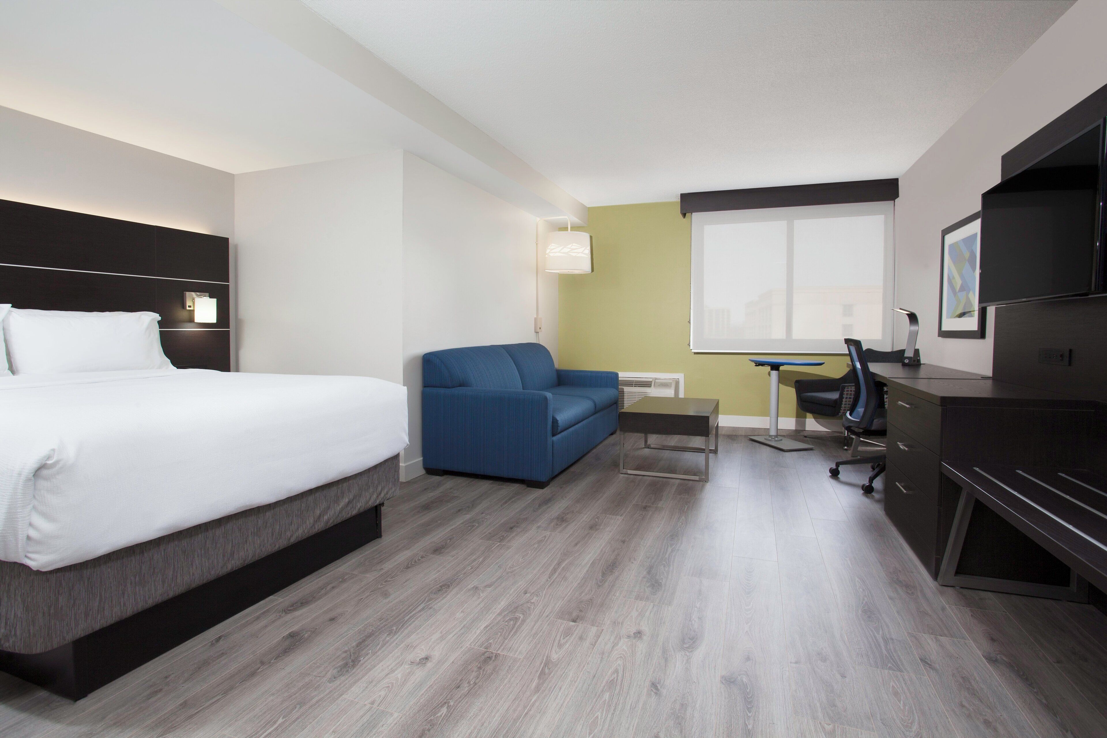 A hotel room with a bed, a blue sofa, a desk with a chair, and a television.