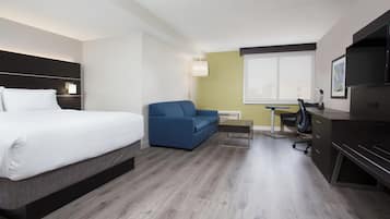 A hotel room with a bed, a blue sofa, a desk with a chair, and a television.