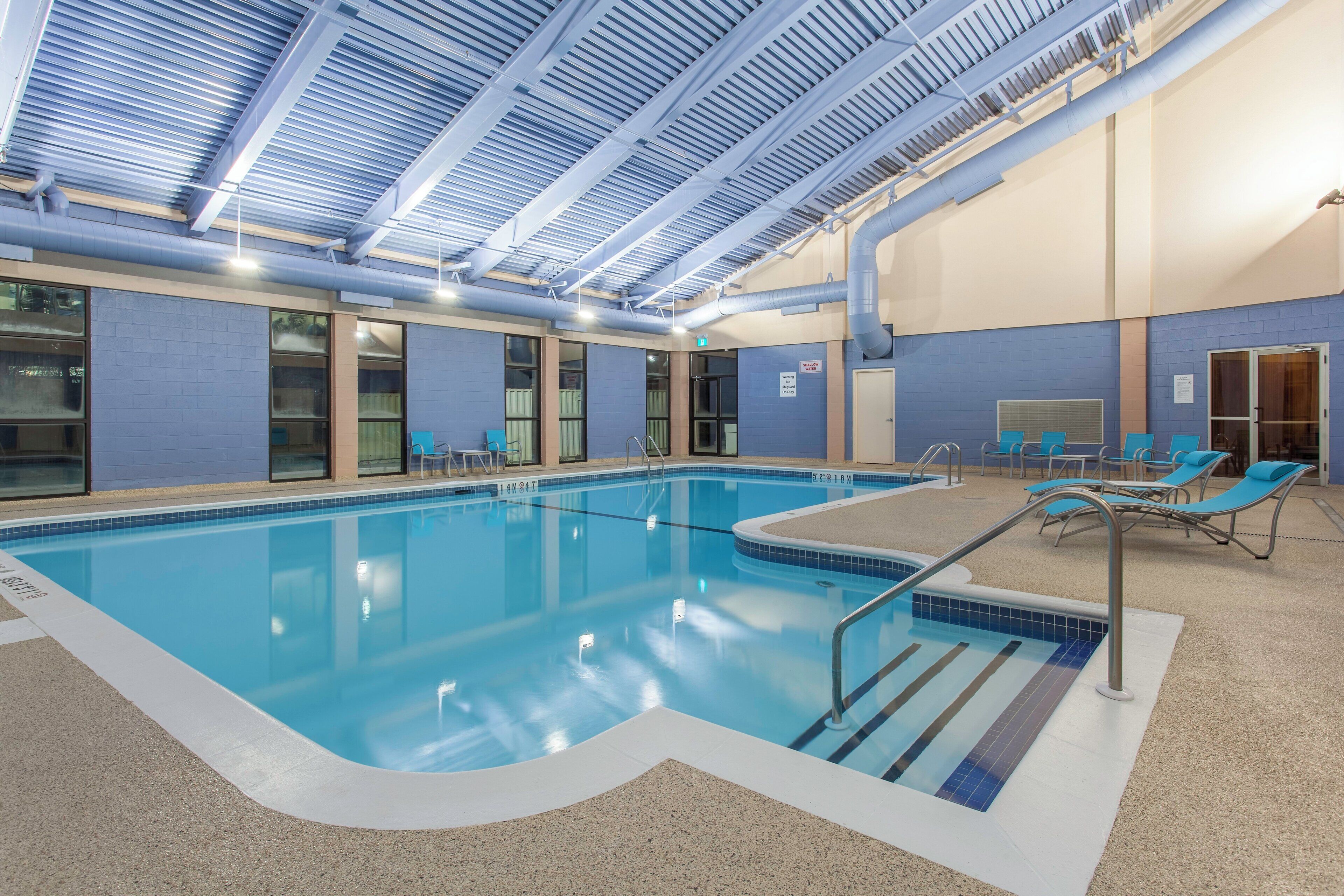 An indoor swimming pool with clear blue water, surrounded by lounge chairs and a ceiling with a grid-like structure.
