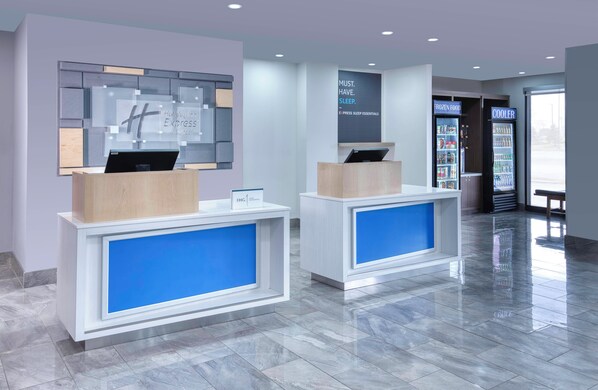 A hotel reception area with two reception desks, a digital display, and a refrigerator vending machine. - Holiday Inn Express & Suites Mississauga-Toronto Southwest by IHG (Mississauga)