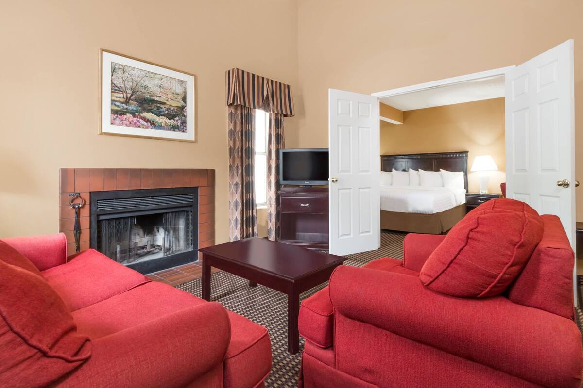 Une chambre d’hôtel avec une cheminée, une télévision, un lit et des meubles recouverts d’un tissu rouge.