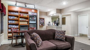Una sala de estar con un sofá marrón, una mesa de centro y una estantería llena de aperitivos y bebidas.