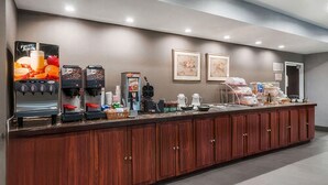 Zona de recepción de hotel con una larga recepción, máquinas de café y diversas opciones de comida y bebida.