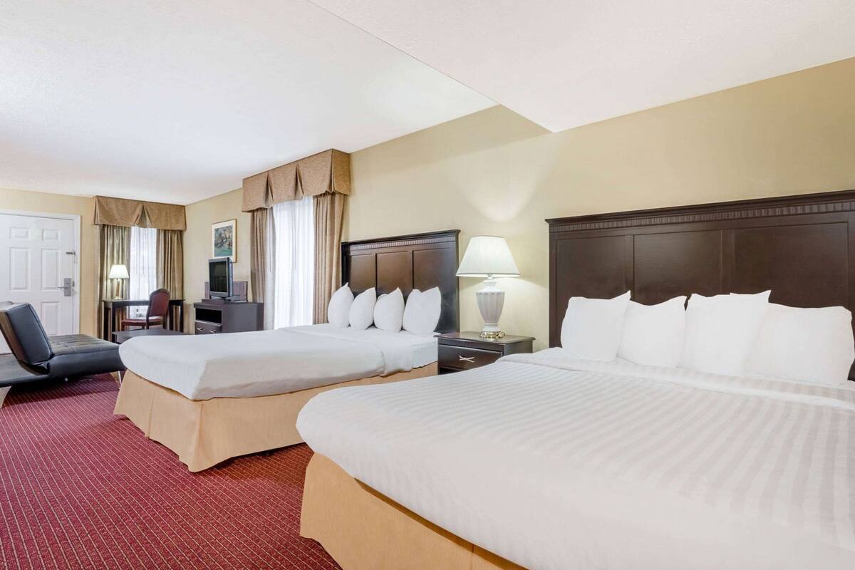 Une chambre d’hôtel avec deux lits, un bureau, une chaise, une télévision et une lampe.