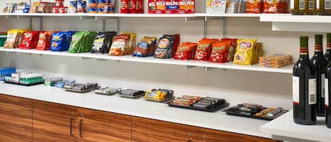 A snack and beverage display in a hotel lobby with various packaged snacks, bottled water, and wine.