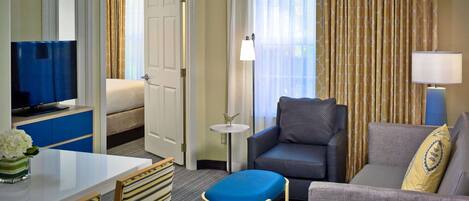 A hotel room with a bed, a TV, a sofa, a small table, and a chair.