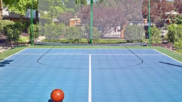 An outdoor basketball court with a net, a basketball, and a clear sky.