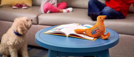 A living room with a sofa, a small round table with a book and a plush toy, and a dog.