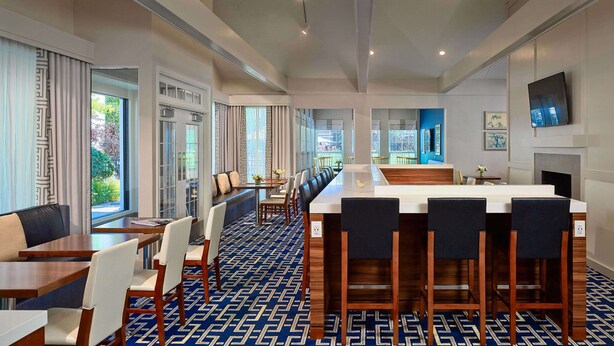 A modern hotel lobby with a long reception desk, seating area, and large windows offering views of the outdoors. - Sonesta ES Suites Cincinnati - Sharonville East (Sharonville)