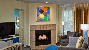 A hotel room with a flat-screen TV, a fireplace, a sofa, a coffee table, and a painting on the wall. - Sonesta ES Suites Cincinnati - Sharonville East (Sharonville)