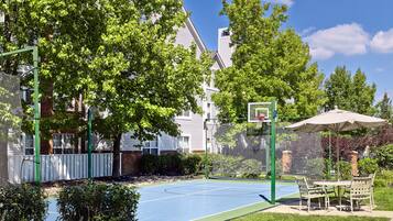 Un terrain de basket en plein air, équipé d’un panier, entouré d’arbres et d’une clôture.