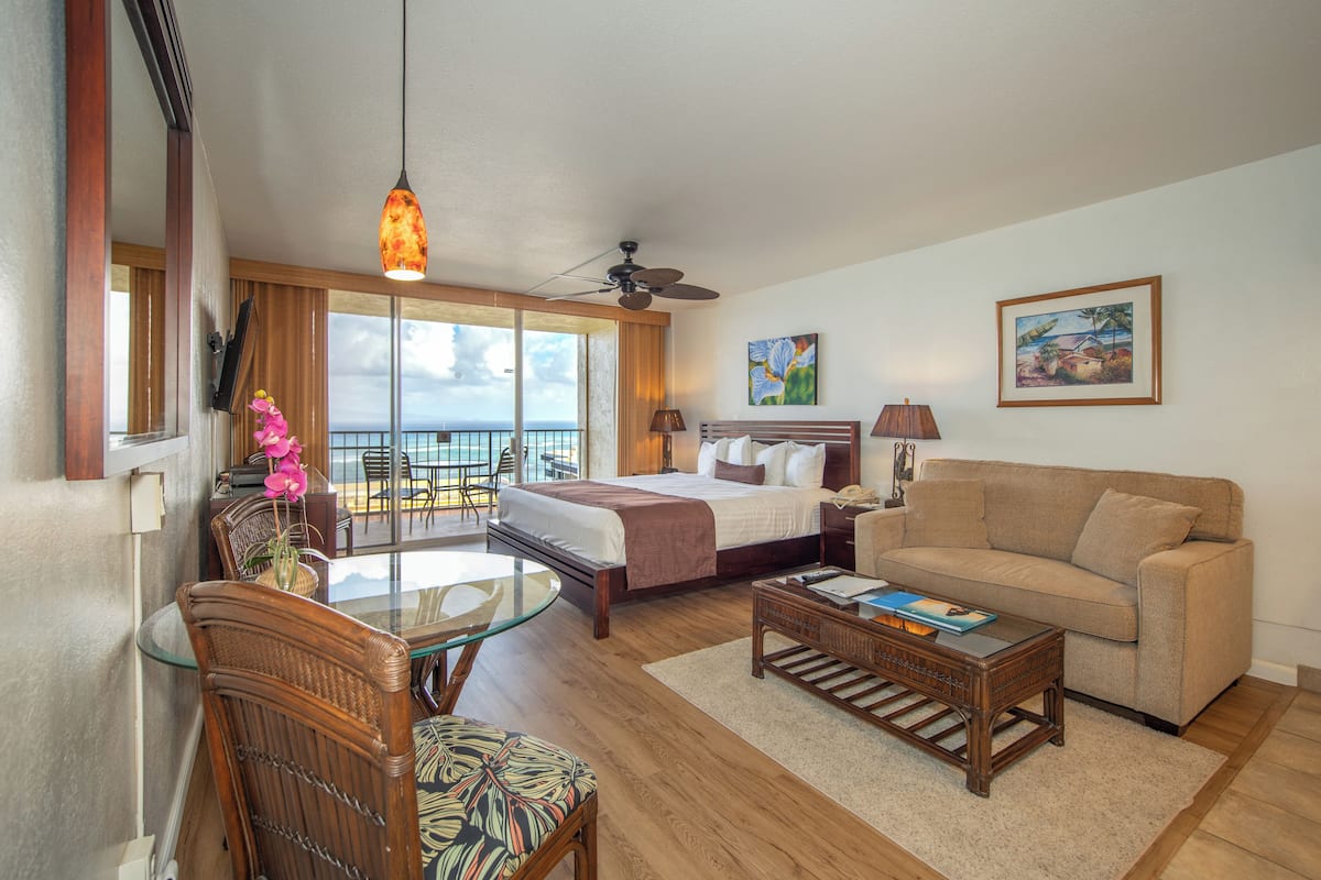 A hotel room with a bed, a sofa, a glass table, and a balcony with a view.