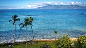 A coastal view with a clear sky, palm trees, and a grassy area with chairs. - Royal Kahana Maui by OUTRIGGER (Lahaina)