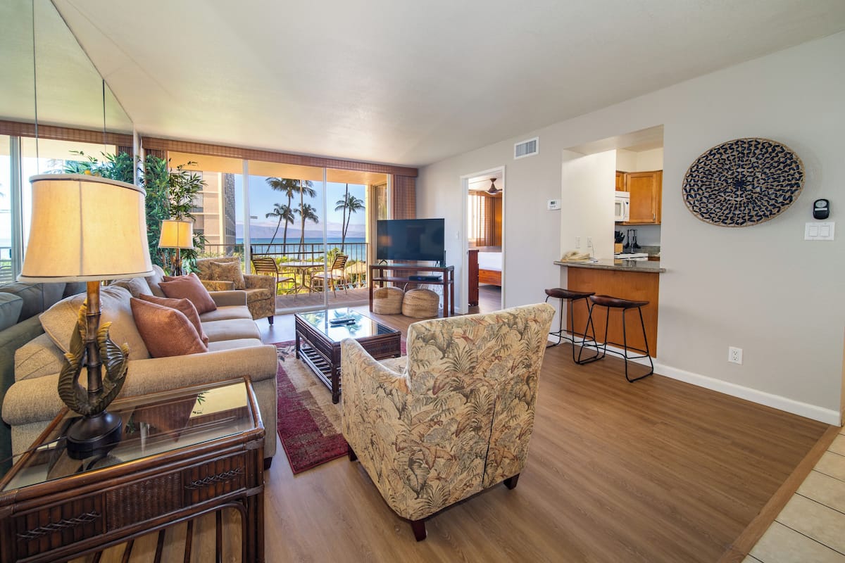 A spacious living room with a large TV, comfortable seating, and a view of the ocean.