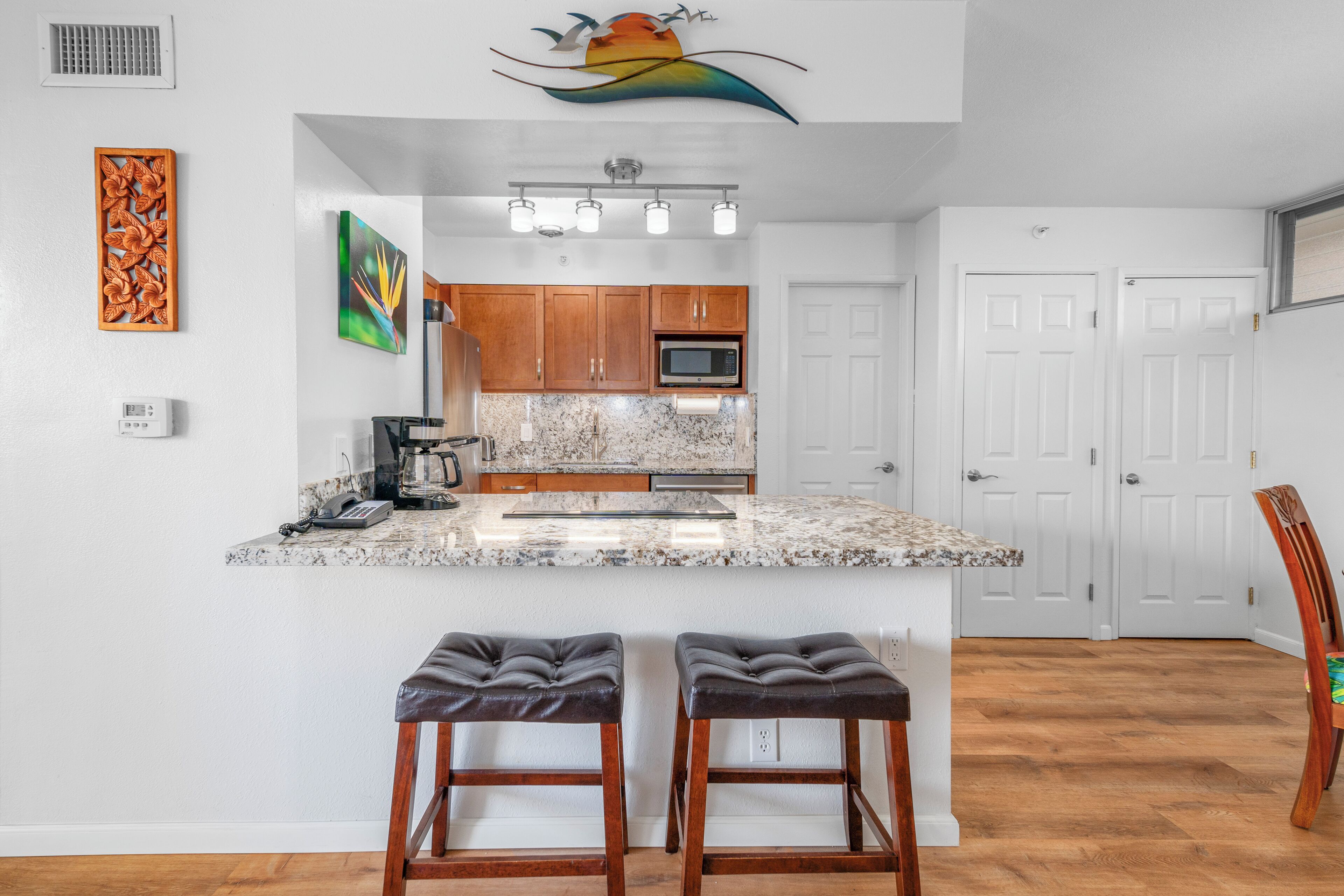 A kitchen with wooden cabinets, a granite countertop, and a built-in microwave. There are two bar stools in front of the counter.