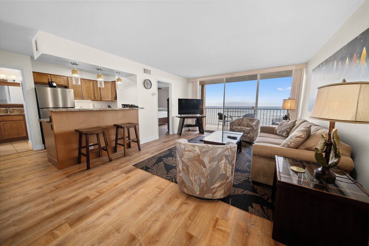 A modern living area with a kitchen, a sofa, a coffee table, and a view of the ocean.