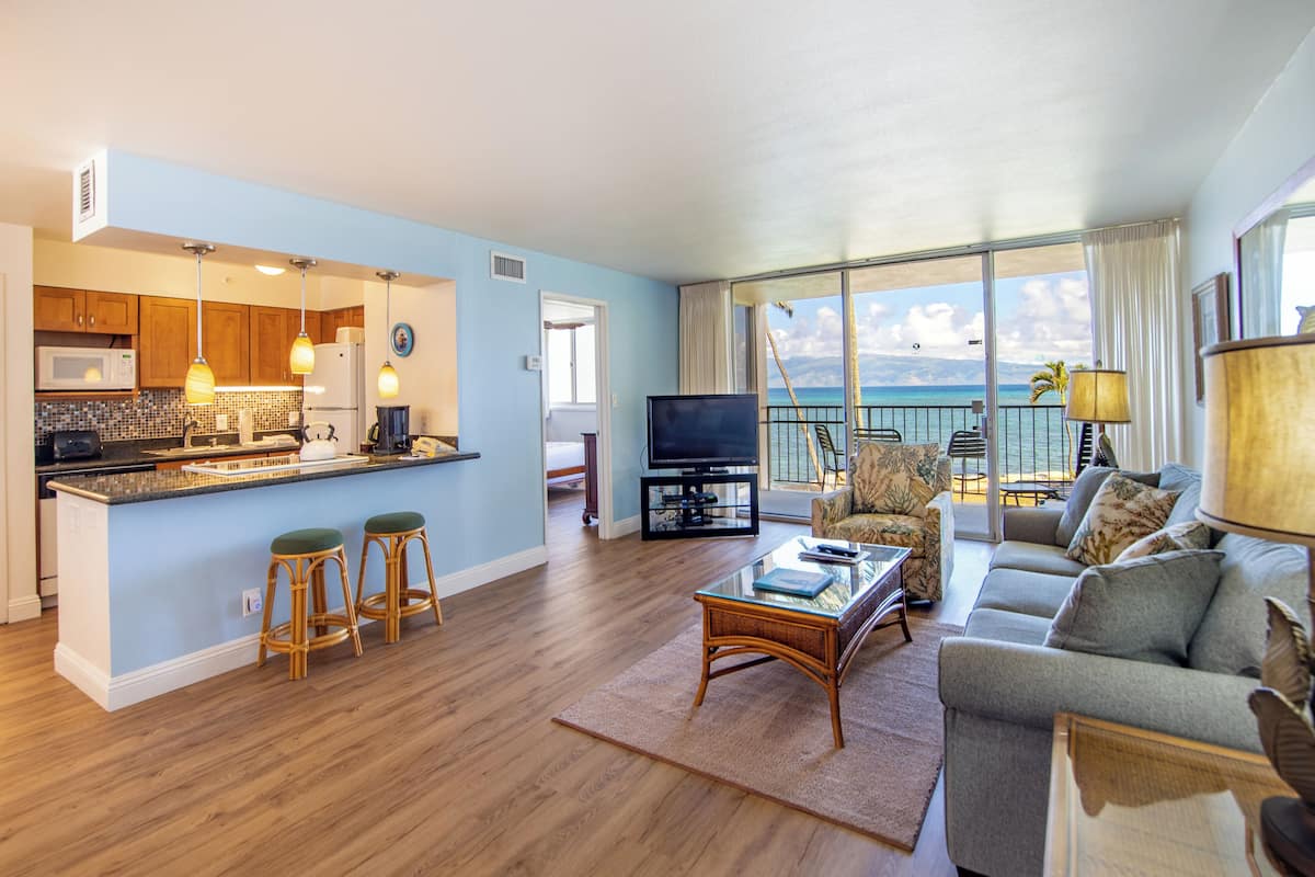 A spacious living area with a kitchen, a balcony with a view of the ocean, and a comfortable seating area.